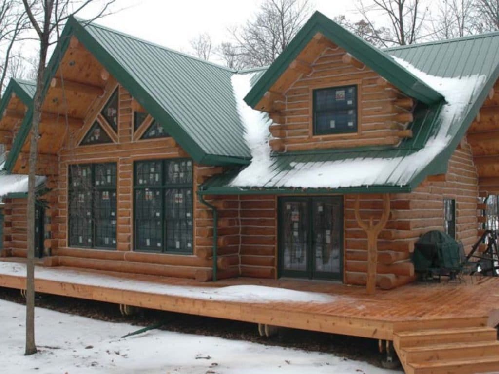 side of log cabin with green roof and picture windows