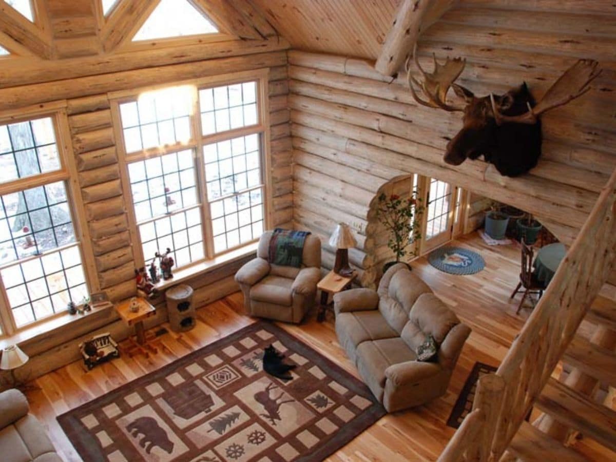 view down into the living room of log cabin with sofa on right and rug in center