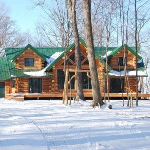log cabin in snowy lot with trees in front