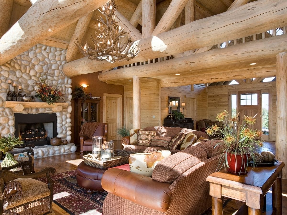 brown leather sofas underneath open log beams and beside stone fireplace in log cabin