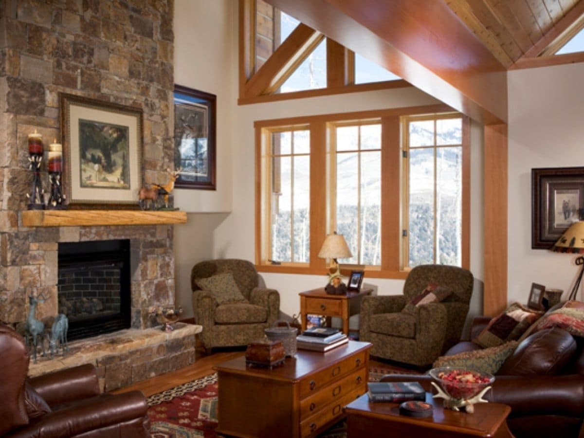 stone fireplace with light brown chairs underneath wall of windows