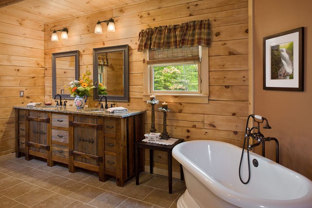white clawfoot bathtub in corner of light wood log cabin with dark wood cabinets under white sinks