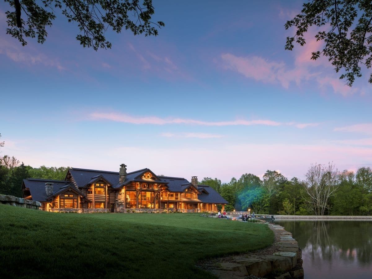 log cabin lit up after dark against treeline with blue sky in background