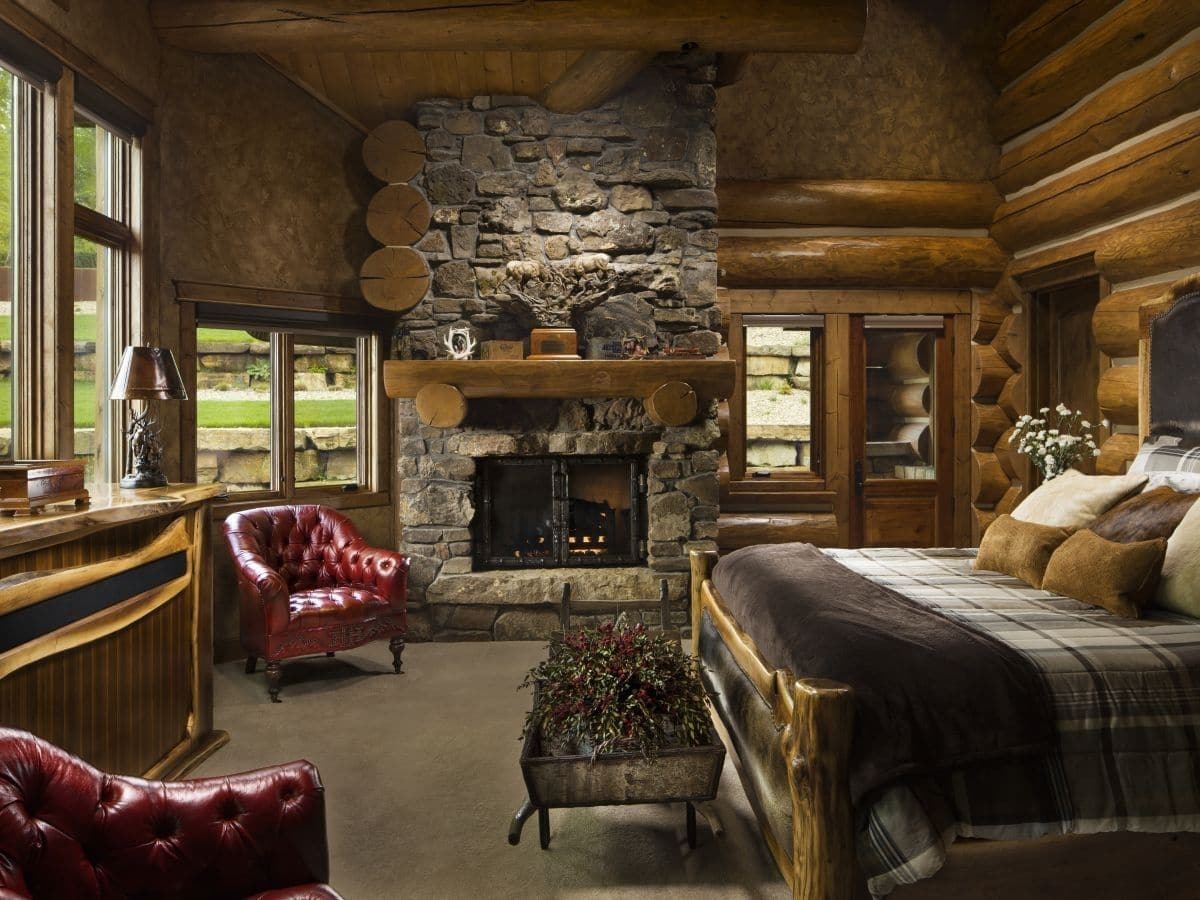 stone fireplace at end of room by log walls and red chair with bed in foreground