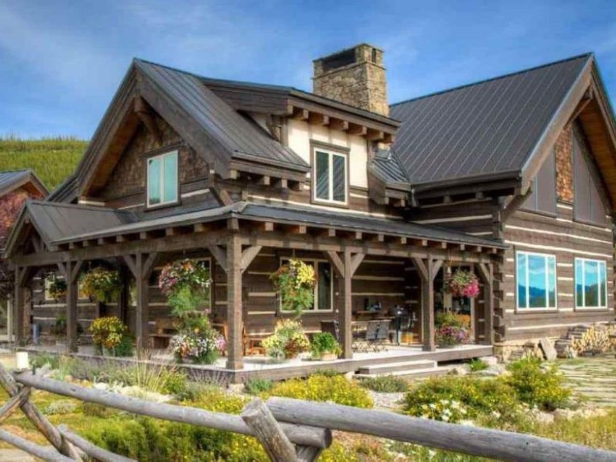 gardens outside fence of dark wood log cabin with white trim