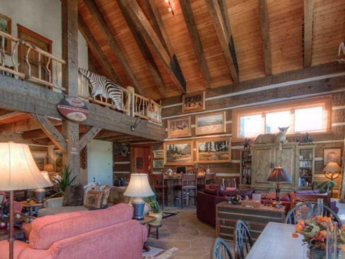 view of kitchen from log cabin living room with pink chair in foreground and red sofa in background