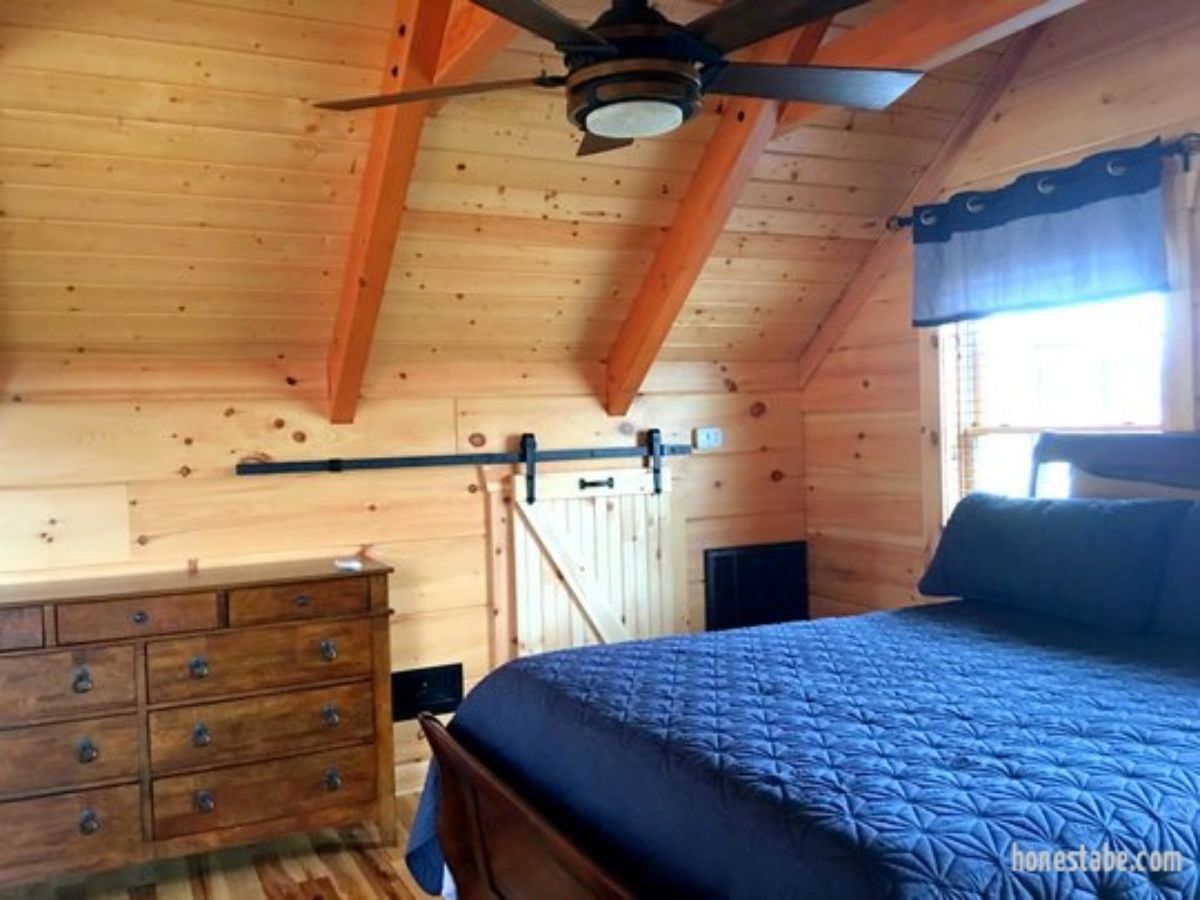 blue bed in log cabin loft bedroom with black ceiling fan