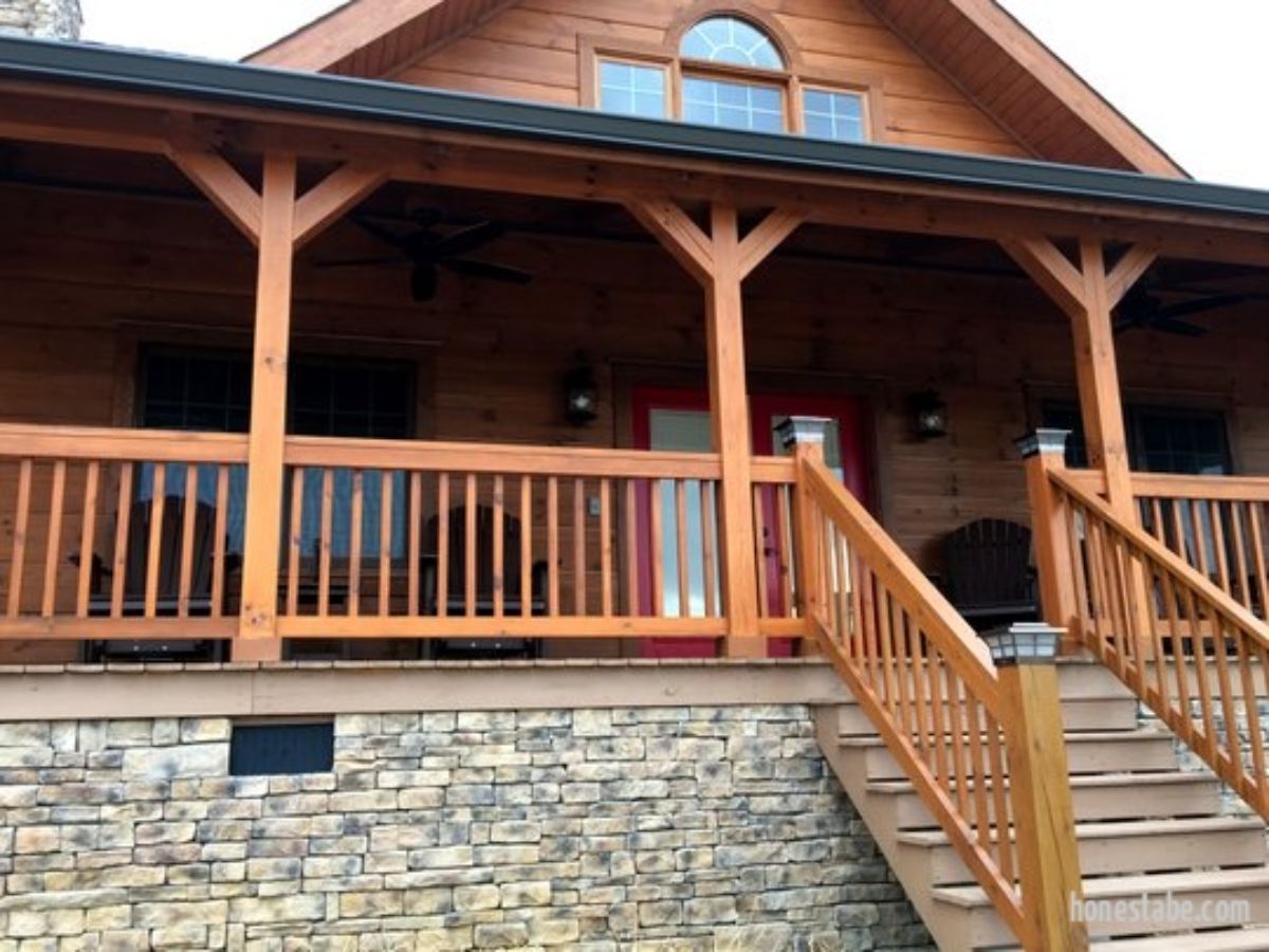 front porch on log cabin with stone base and wood railing