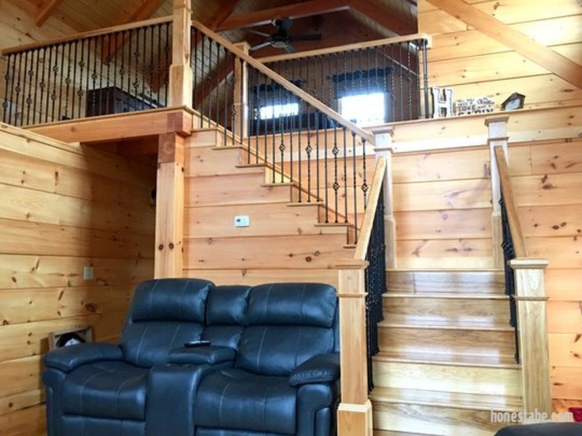 black leather loveseat against stairs to loft in log cabin