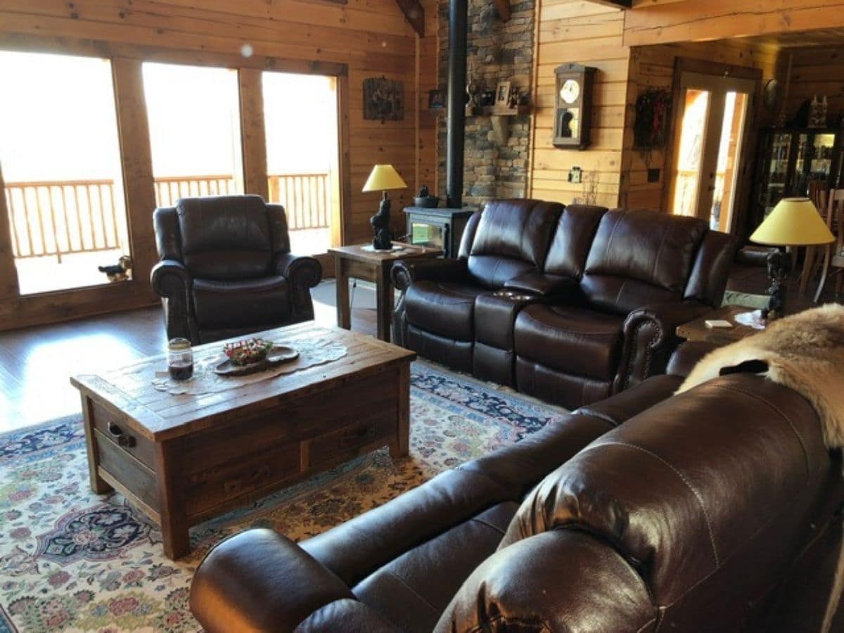 wooden coffee table in middle of brown leather reclining sofas in living room of log cabin