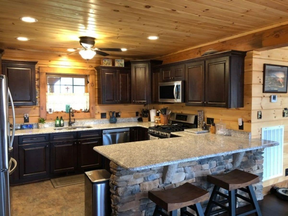 kitchen with stone backing on cabinets facing forward and dark wood cabinets with stainless steel appliances