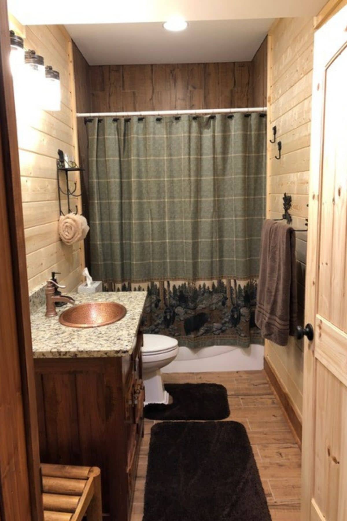 green shower curtain on shower in back of bathroom with wood cabinet under brass sink