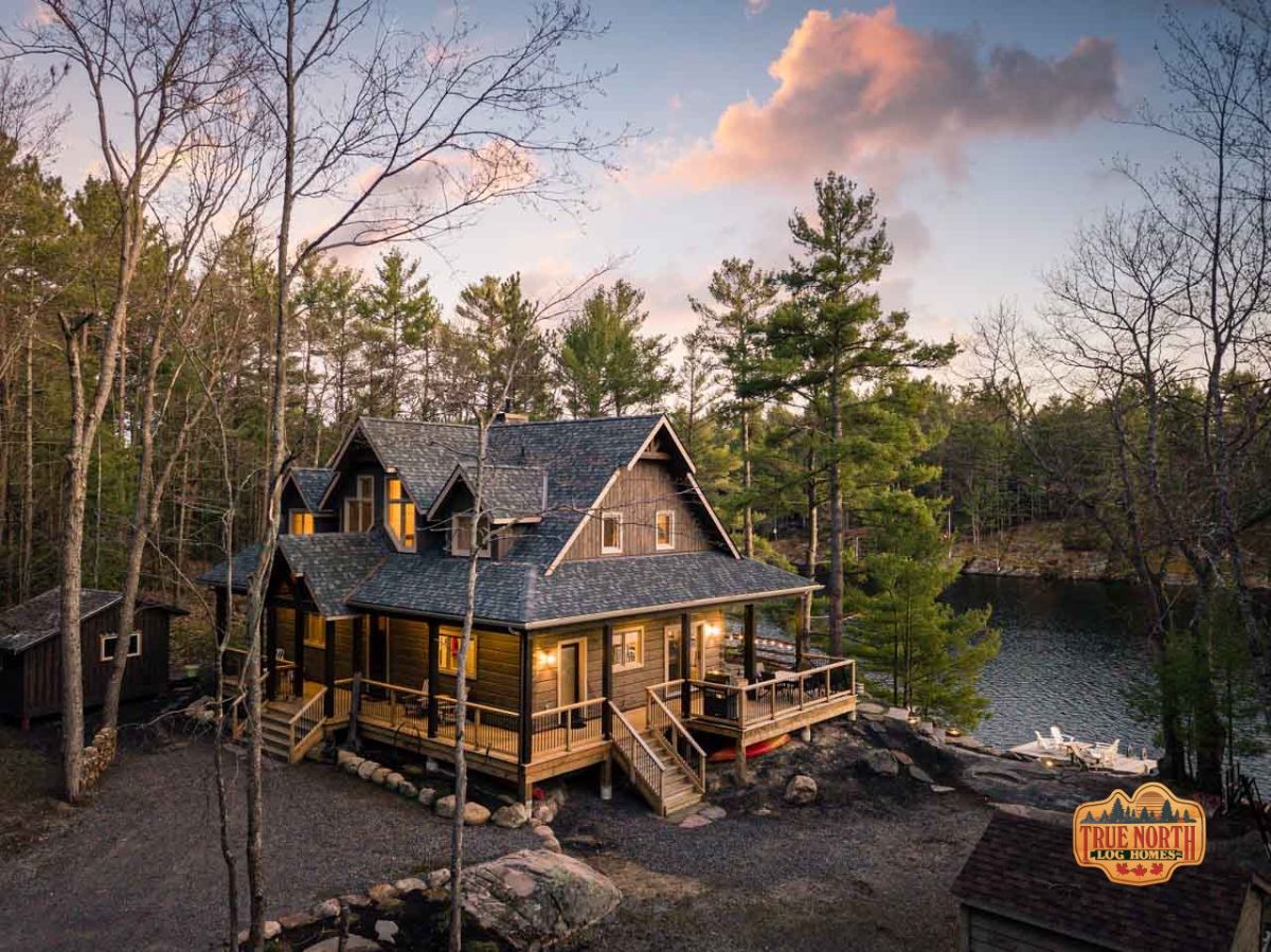 two story log cabin with wrap around porch and lake in background