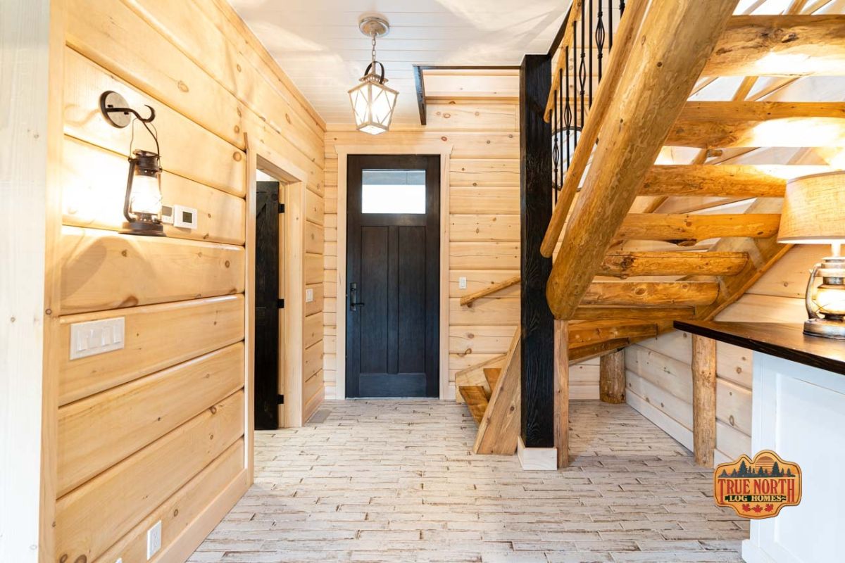 black door of entry to log cabin with light wood walls next to stairs