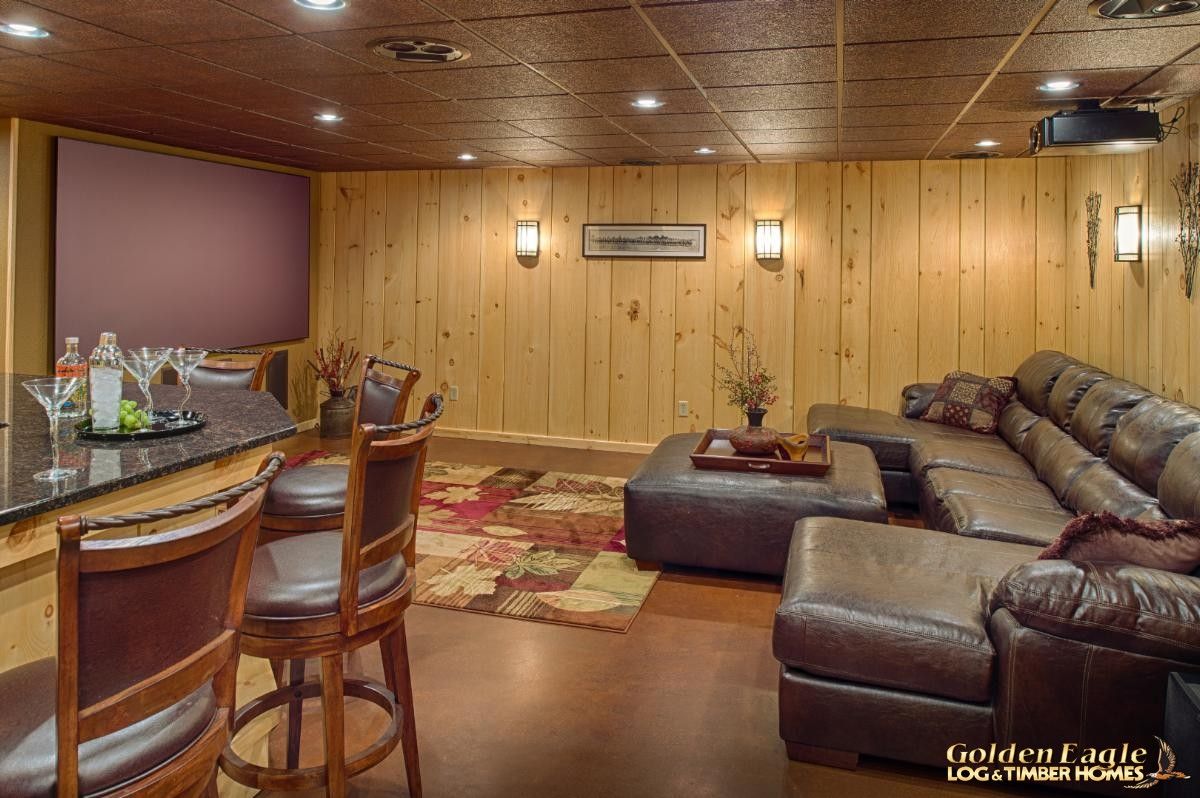 sofa against right wall with table and chairs in foreground on left of log cabin basement