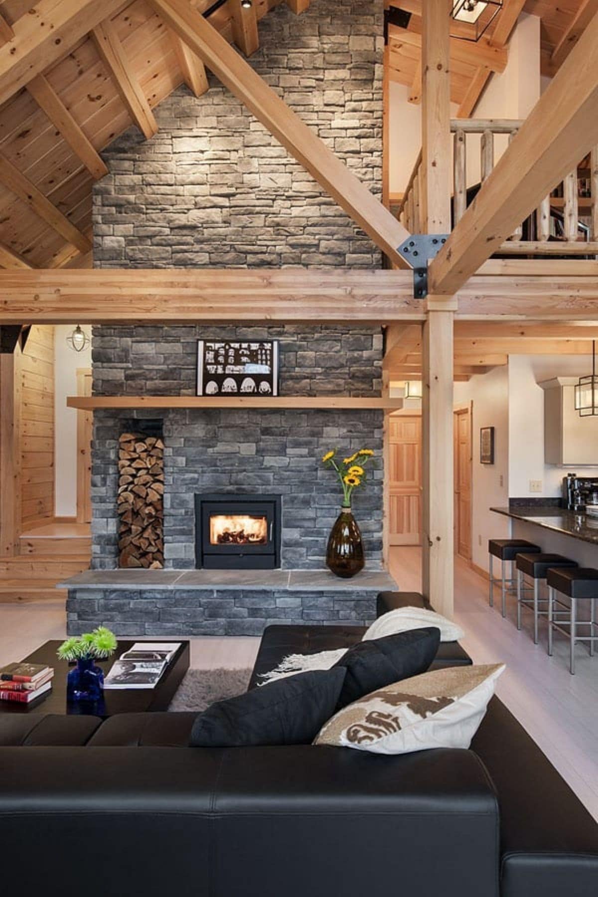 stone fireplace against wall with light wood beams and black sofa