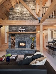 stone fireplace against wall with light wood beams and black sofa