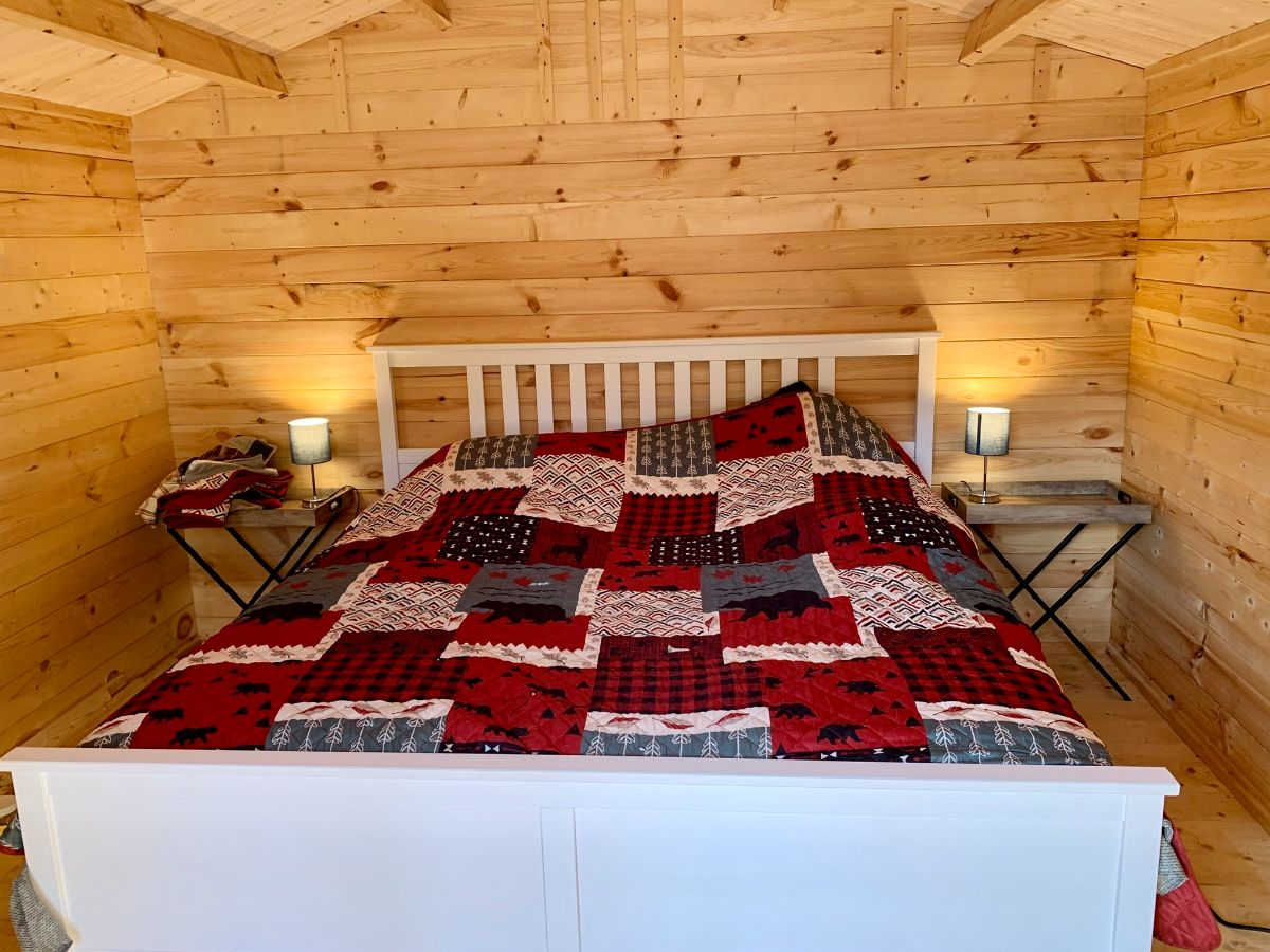 red and black quilt on bed in small log cabin