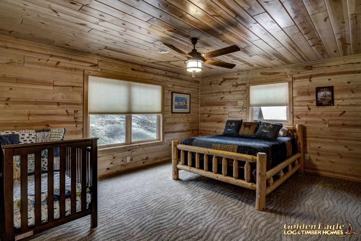 bed against far wall with wooden crib against front left wall and windows between