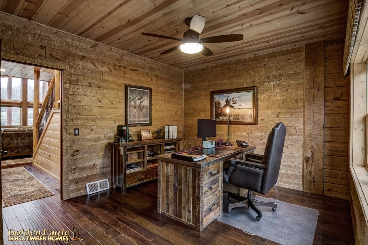 black office chair behind desk on light gray rug in log cabin office