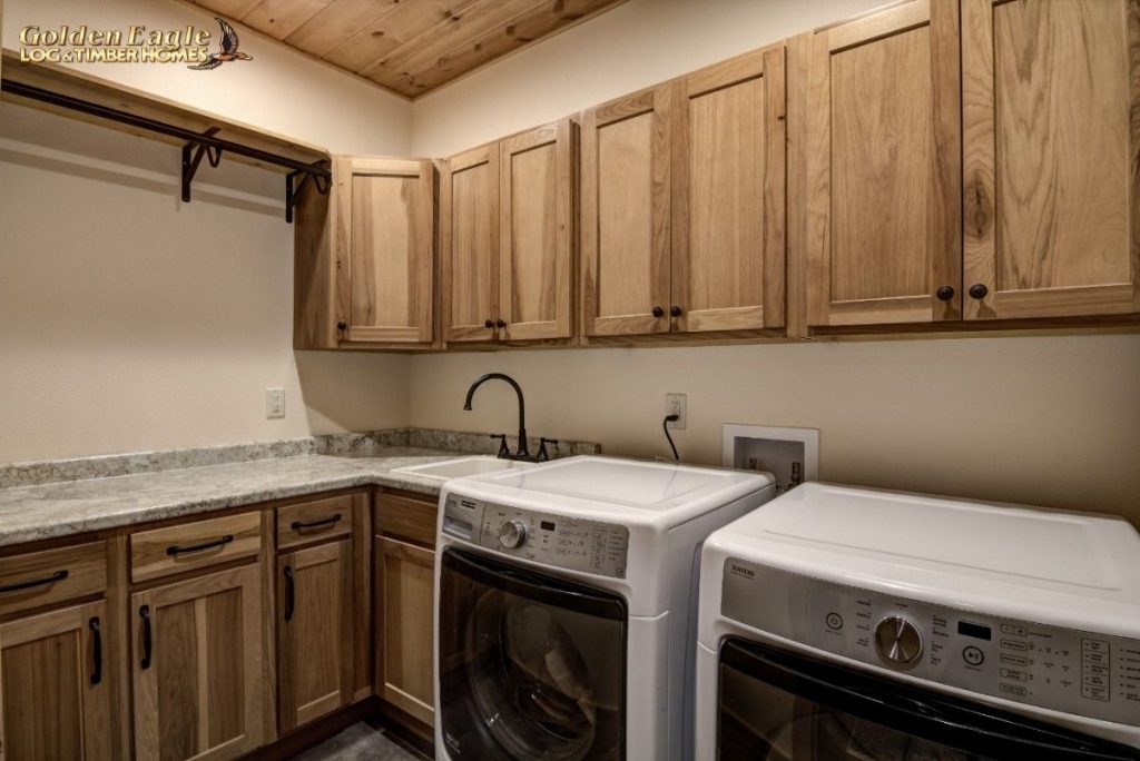 white and black washer and dryer under light wood cabinets in log cabin laundry room