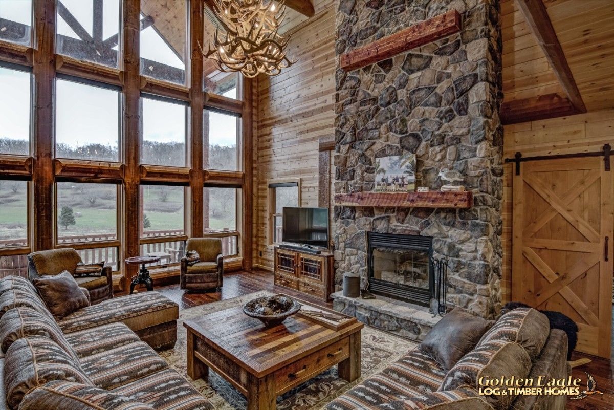 stone fireplace against back wall of log cabin with windows on left wall of image