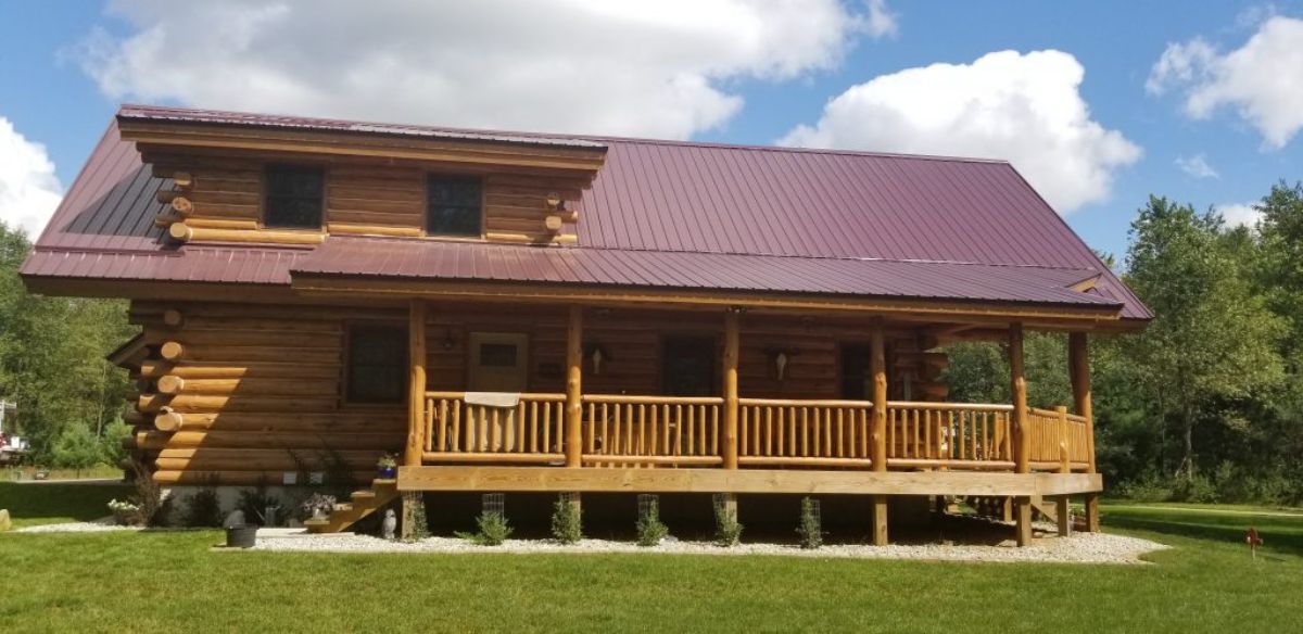 side of log cabin with maroon roof and porch on side