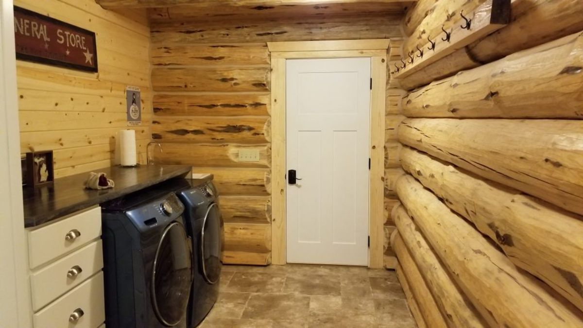 log cabin laundry room with black washer and dryer on left side and white door at end