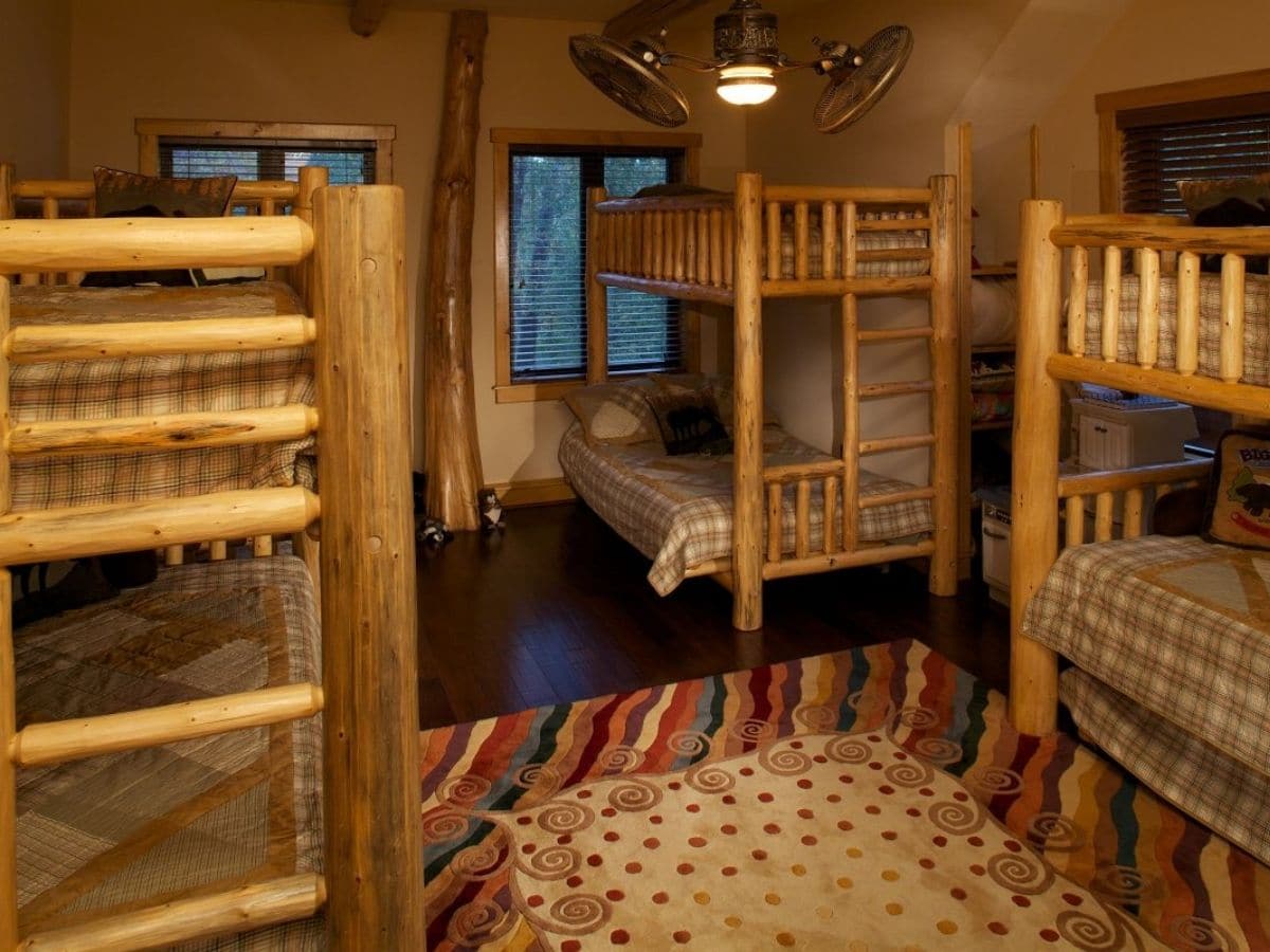 wooden bunk beds in log cabin bedroom with colorful rug in center of floor