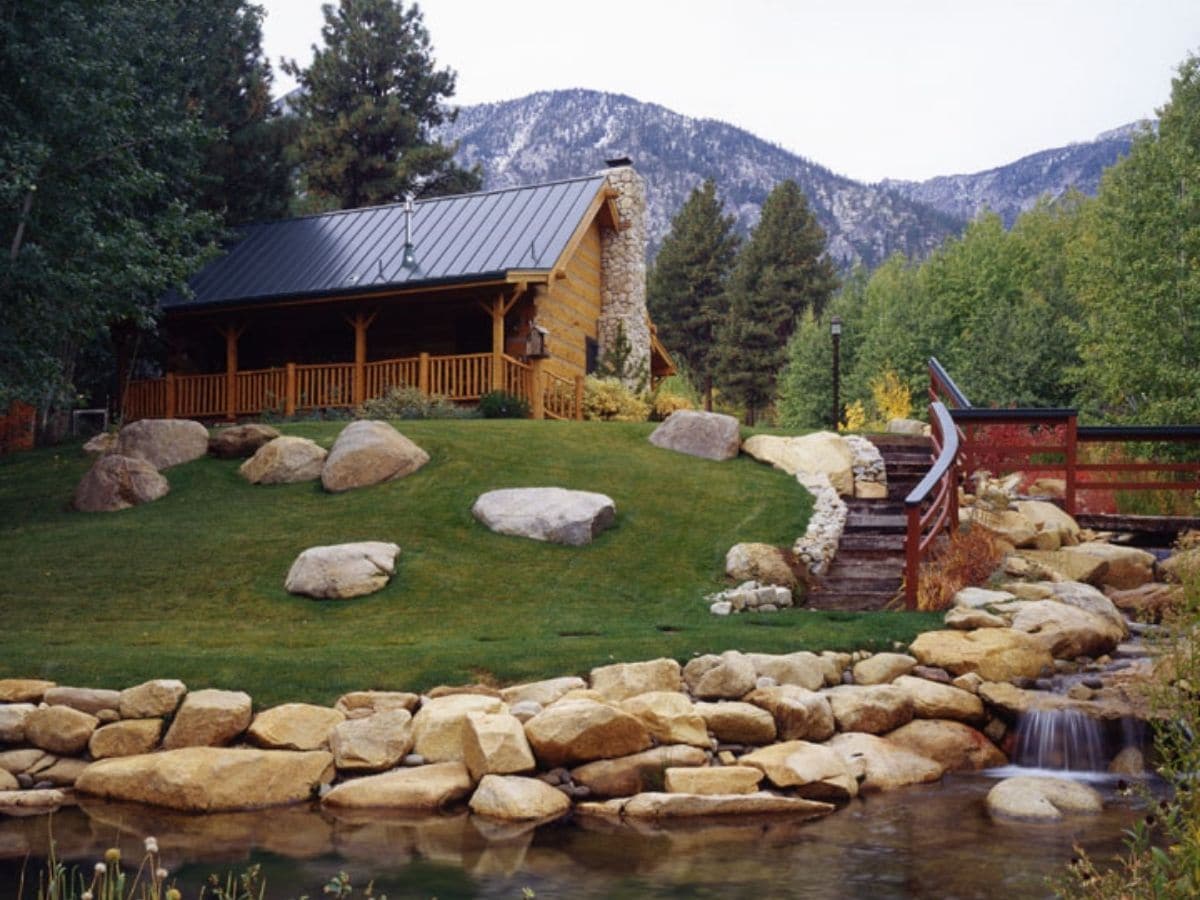 log cabin on top of hill with rock creek in foreground