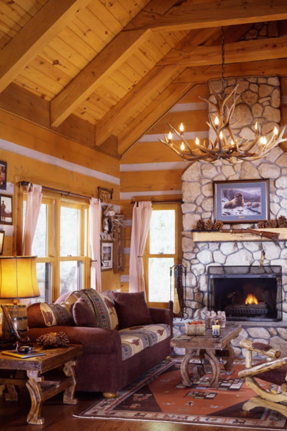 stone fireplace with wooden mantle inside log cabin with antler chandelier in middle of room