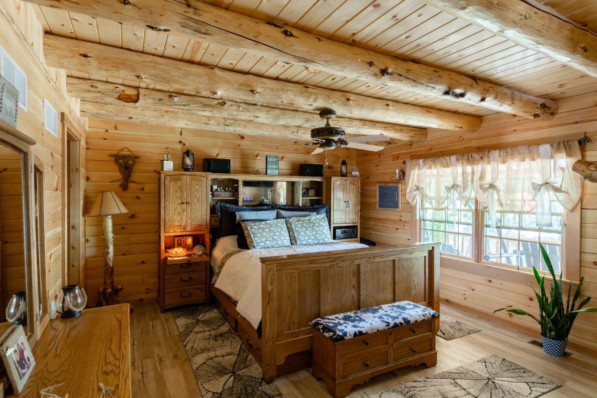 bed with shelving against headboard in log cabin with windows on right