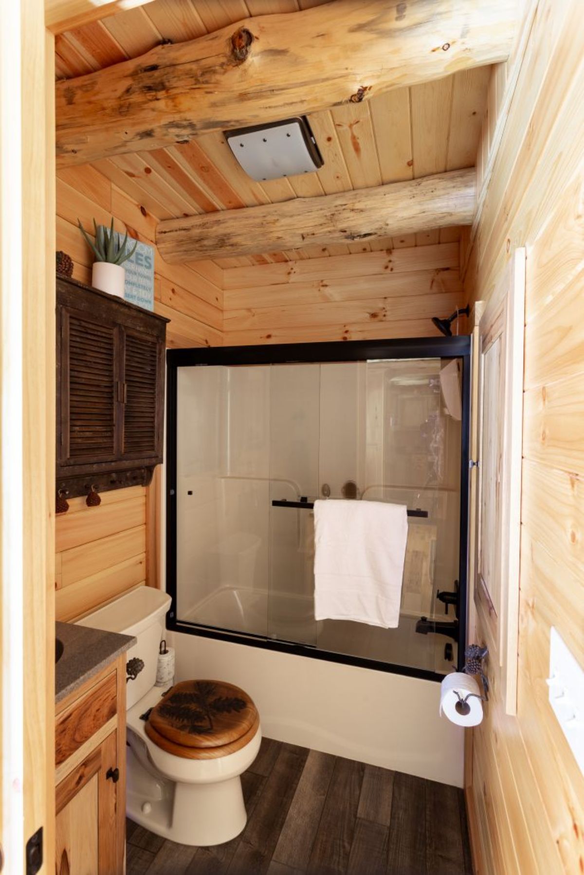 white bath and shower combination with black trim in log cabin bathroom