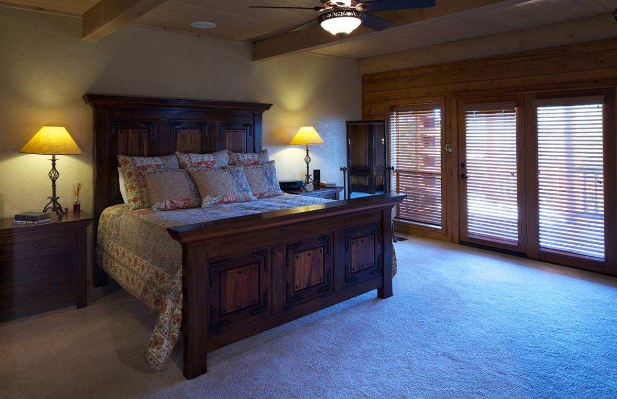 sleigh bed against wall with ceiling fan above and french doors on the right of room