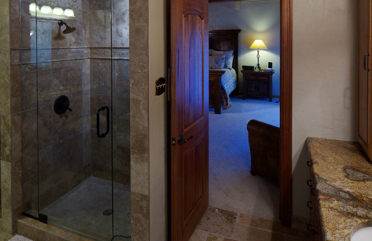 glass shower on left of bathroom door with dark wood door open to bedroom