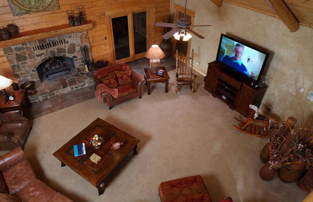 view into living room of log cabin from loft showing dark wood cofee table and entertainment center
