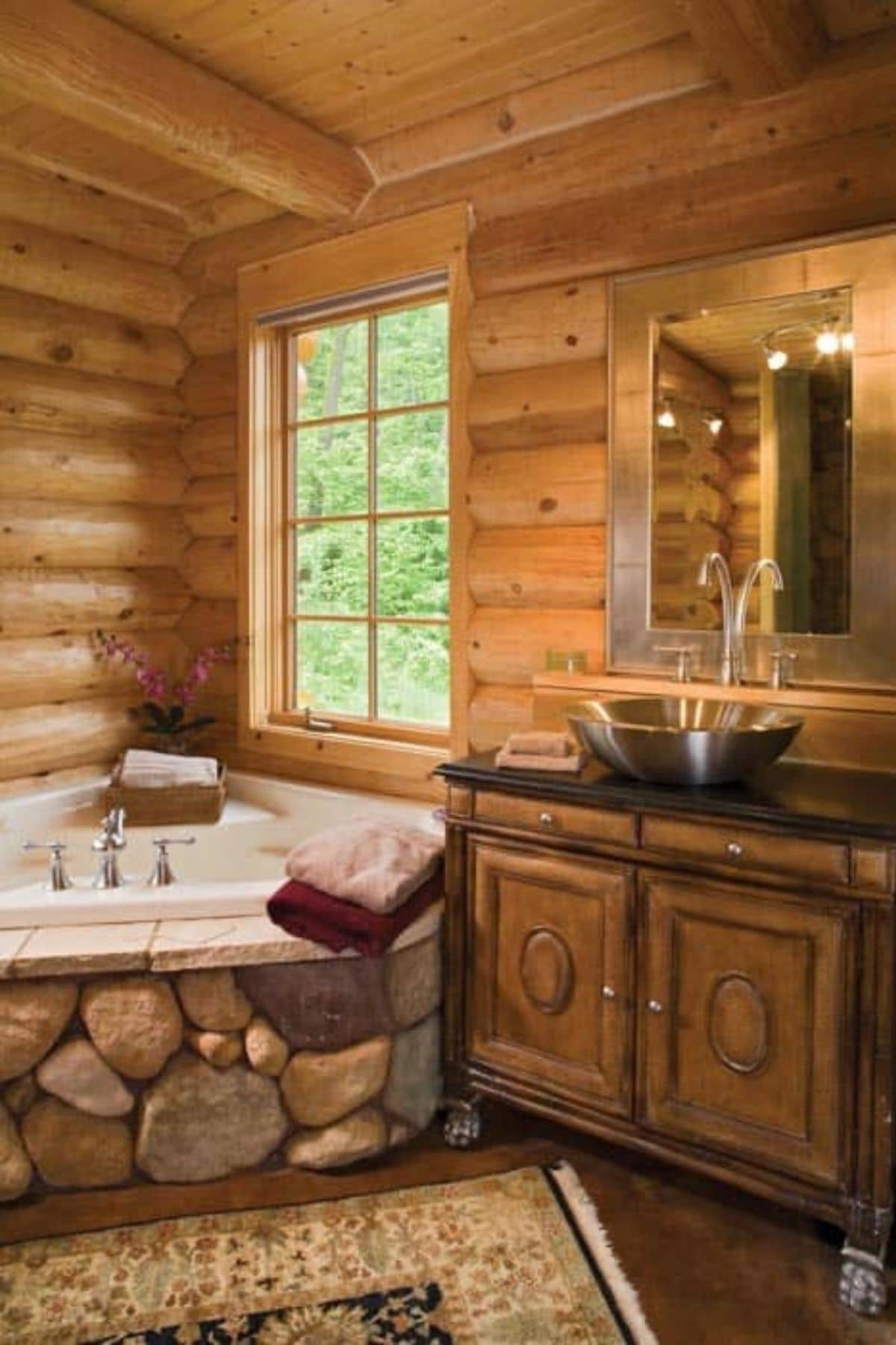 bathroom with soaking tub in corner surrounded by stones net to wood vanity with silver bowl sink