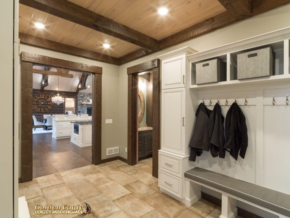 entryway with coat rack above gray bench seat in log cabin