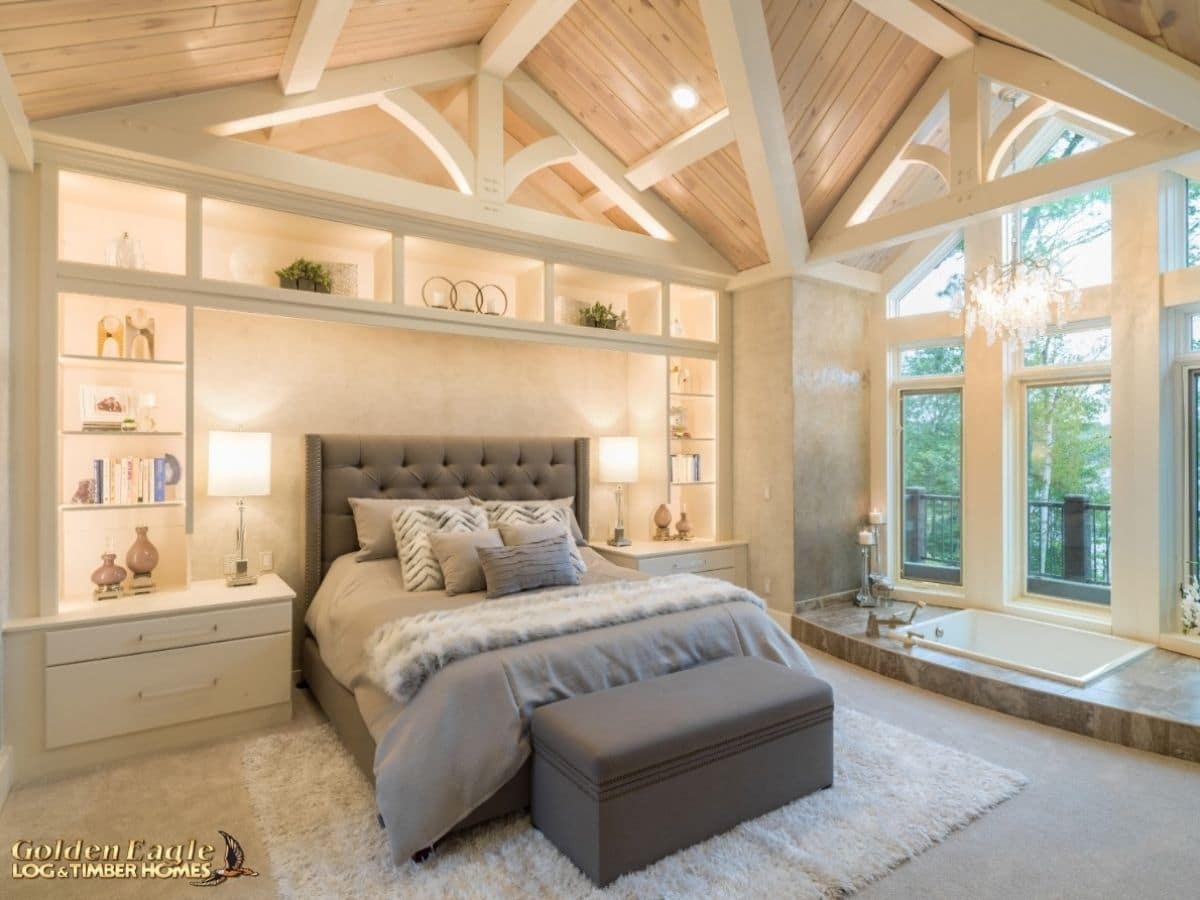 gray and white bed in whitewashed bedroom with white beams and large windows