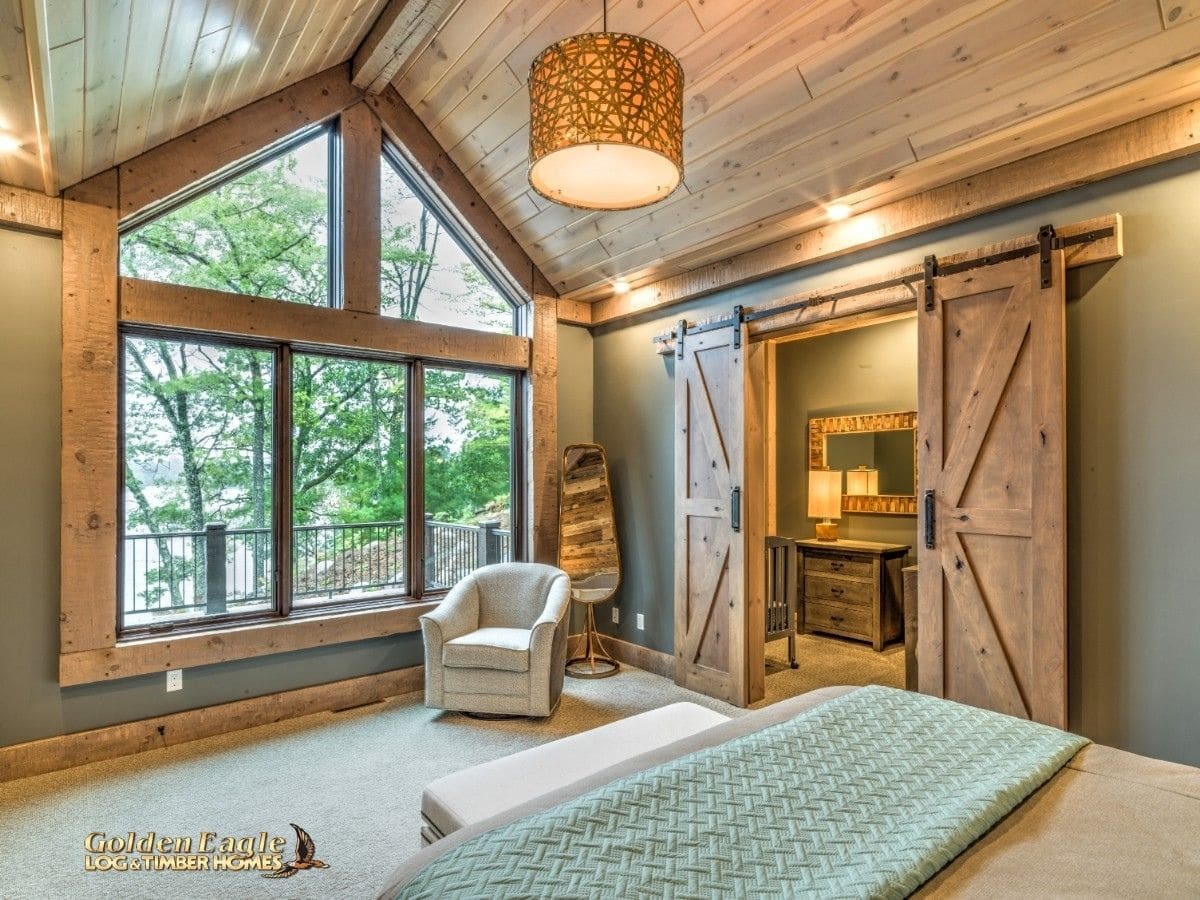 bedroom with light wood walls and picture window by bed with gdeen blanket