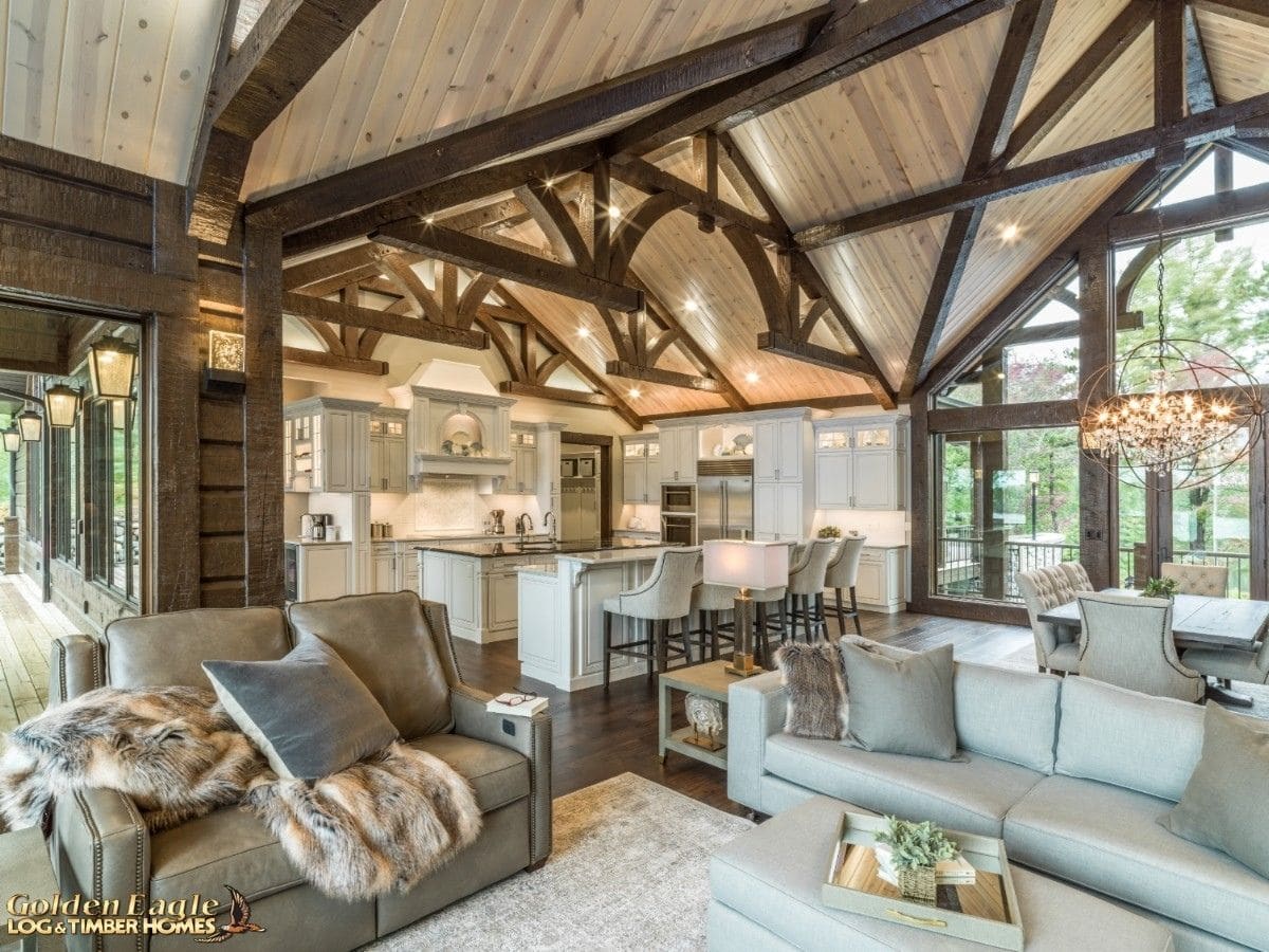 sofas in front of white kitchen island below dark wood beams of log cabin