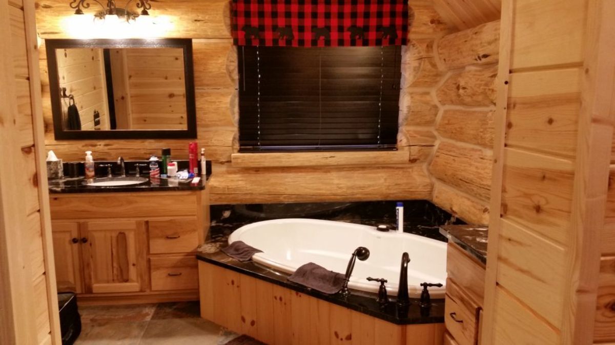 white soaking tub in corner of log cabin bathroom with black tile surround