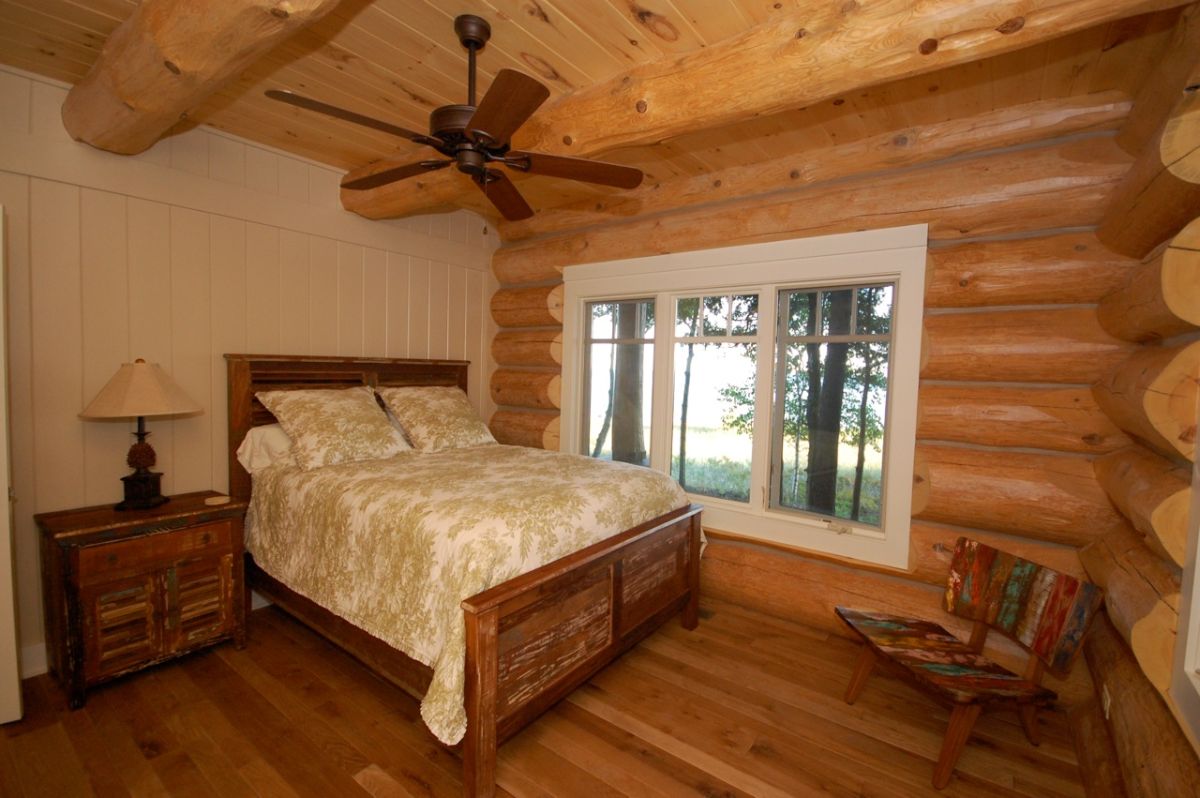 log wall on right with white shiplap wall behind bed on left