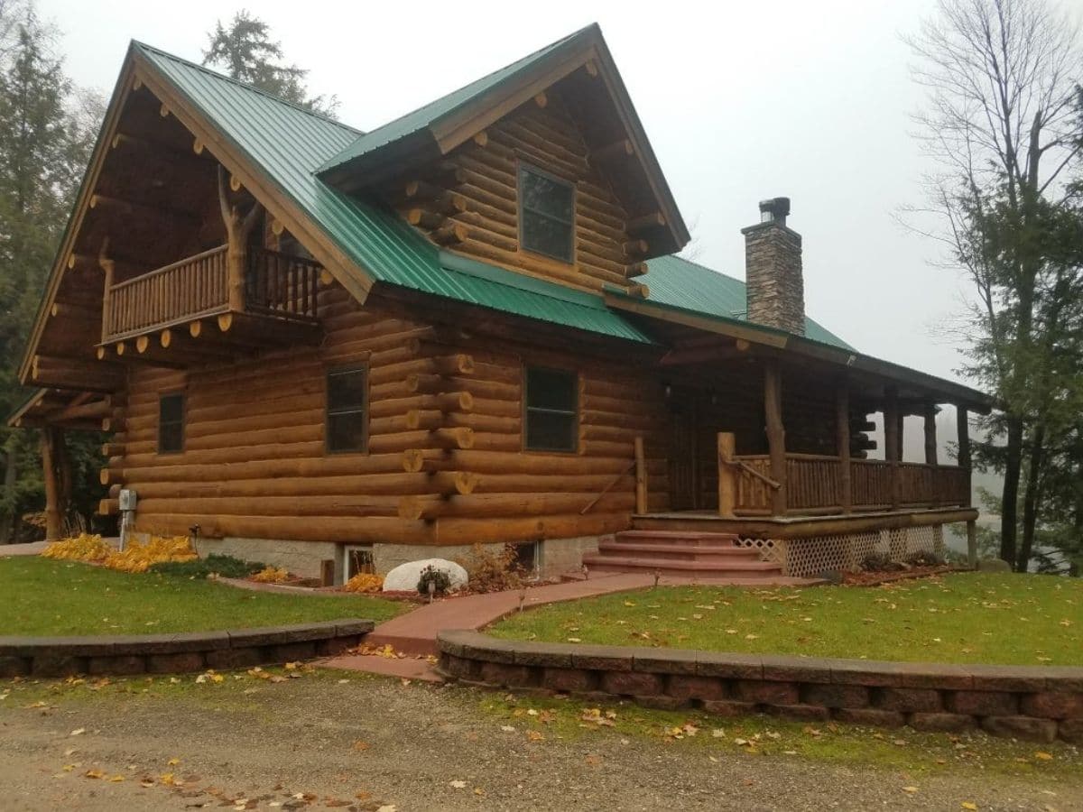 front door of log cabin with green roof and small porch