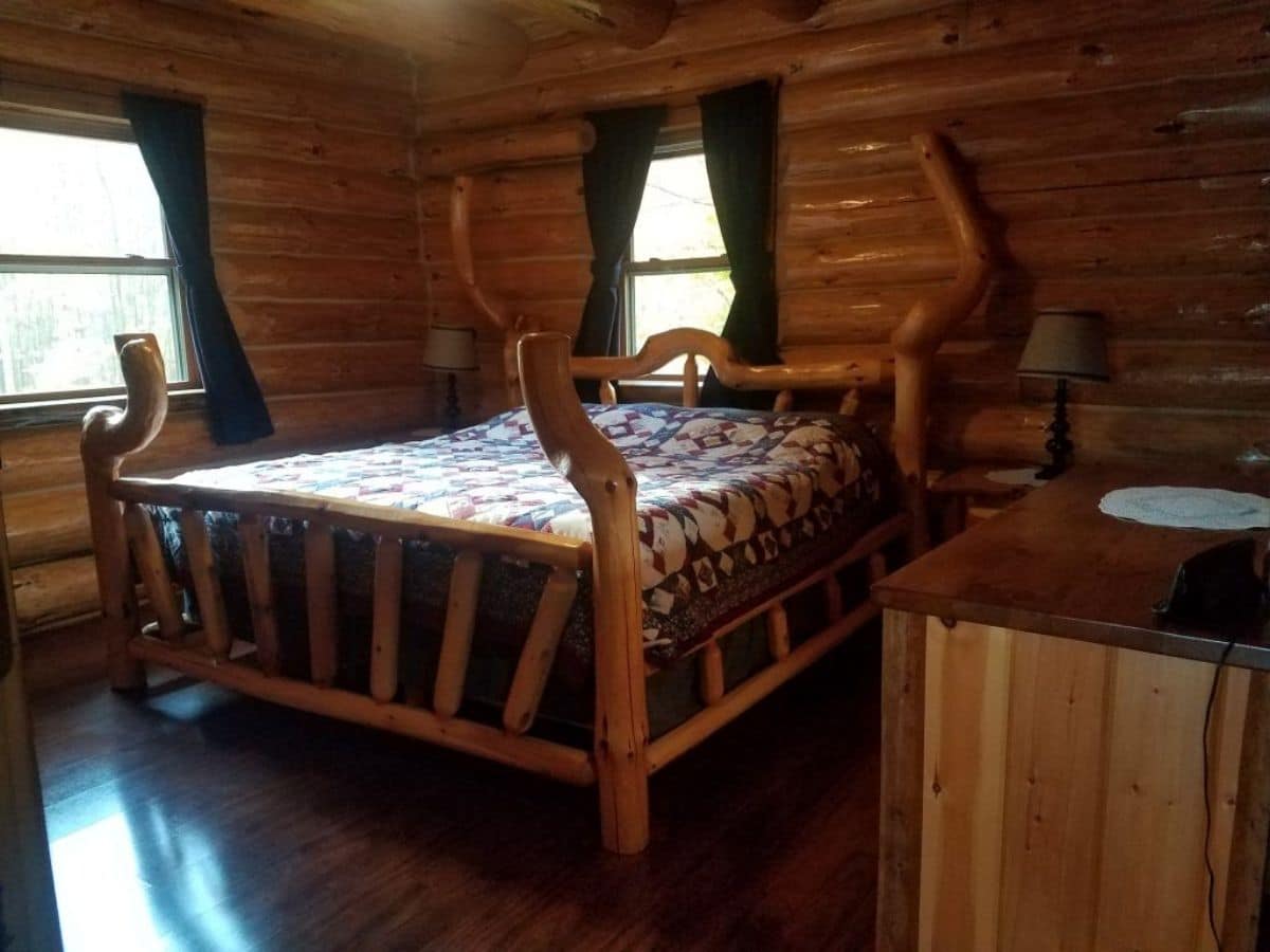 log bedframe on bed against log cabin walls with green curtains over windows