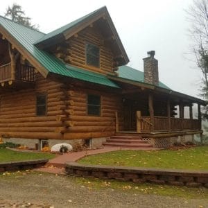 front door of log cabin with green roof and small porch