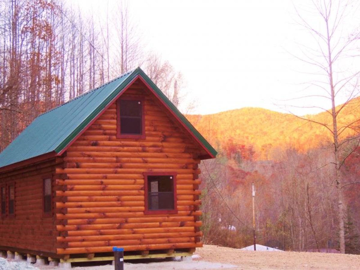 sunset behind log cabin with green roof and two windows on the end