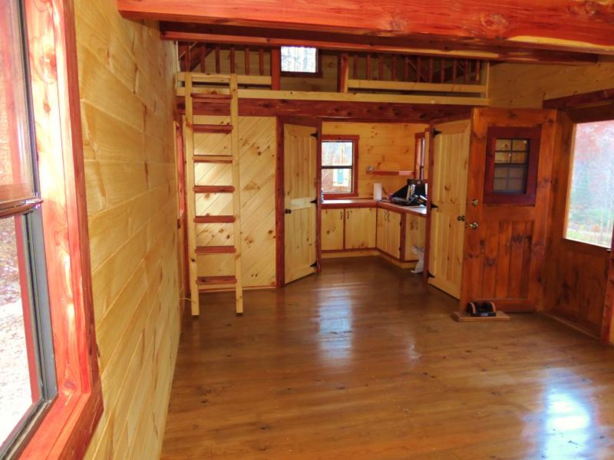 light wood walls with stained trim inside log cabin and wood ladder on back left
