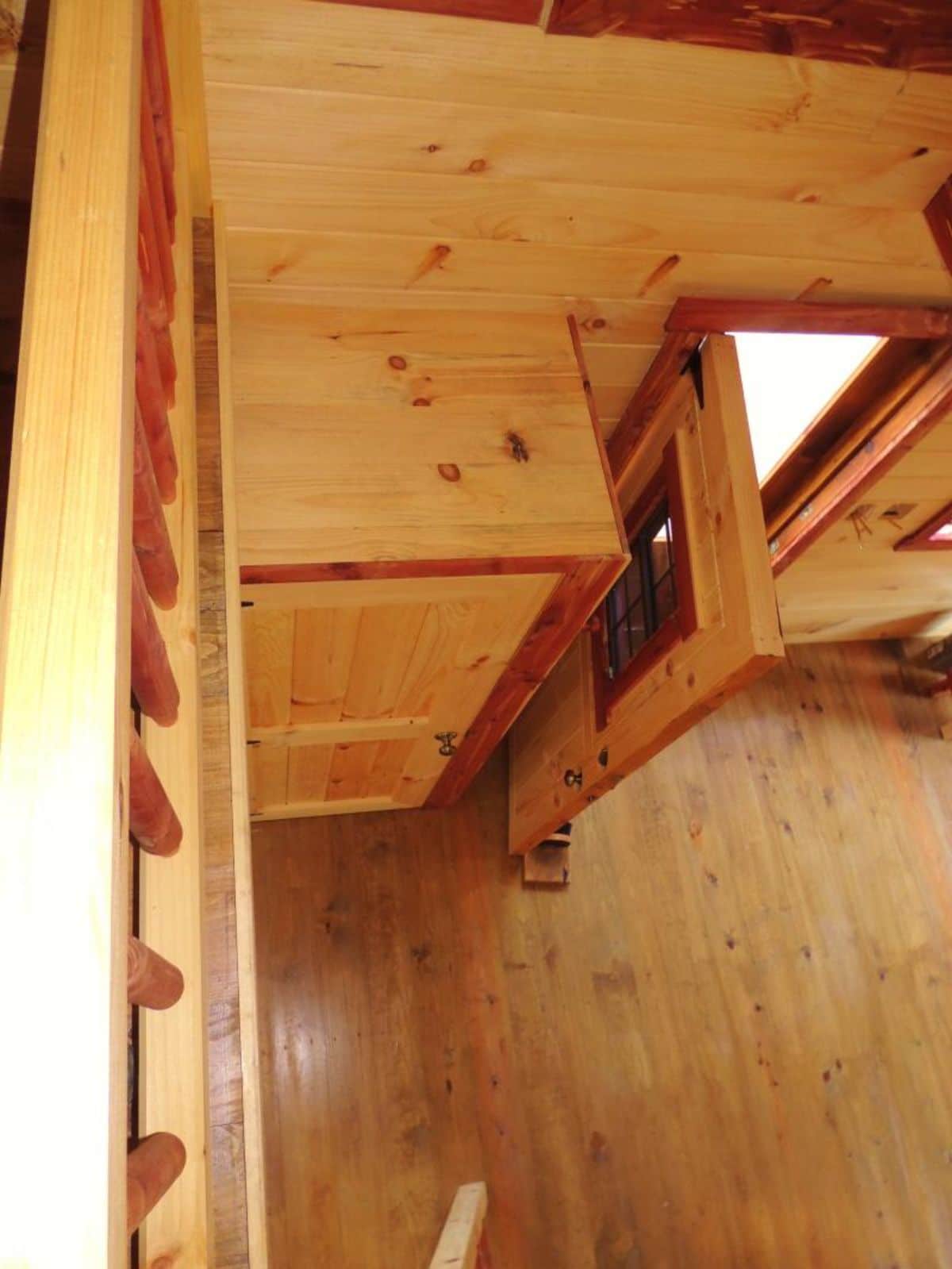 view down into main floor of log cabin by front door that is open with cabinet to left of image