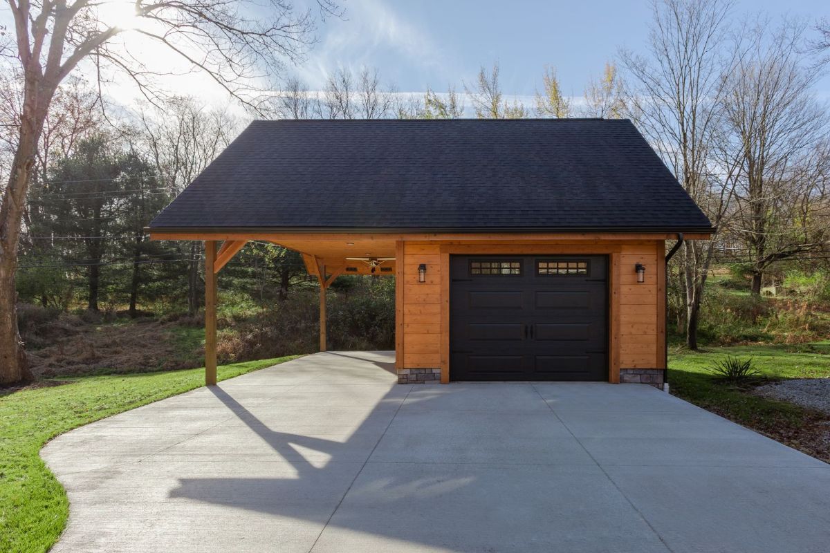 brown garage door on detached log garage and carport with concrete driveway